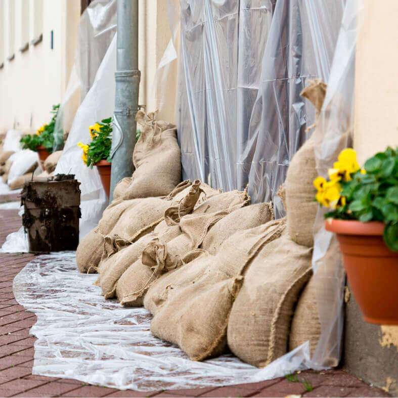 MIt Sand gefüllte Säcke vor einer Haustür zum Schutz vor Hochwasser. Wer zahlt? Die Hausrat- oder Elementarversicherung?