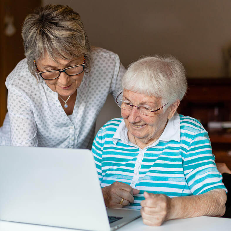 Tochter erklärt ihrer älteren Mutter die Nutzung des Laptops